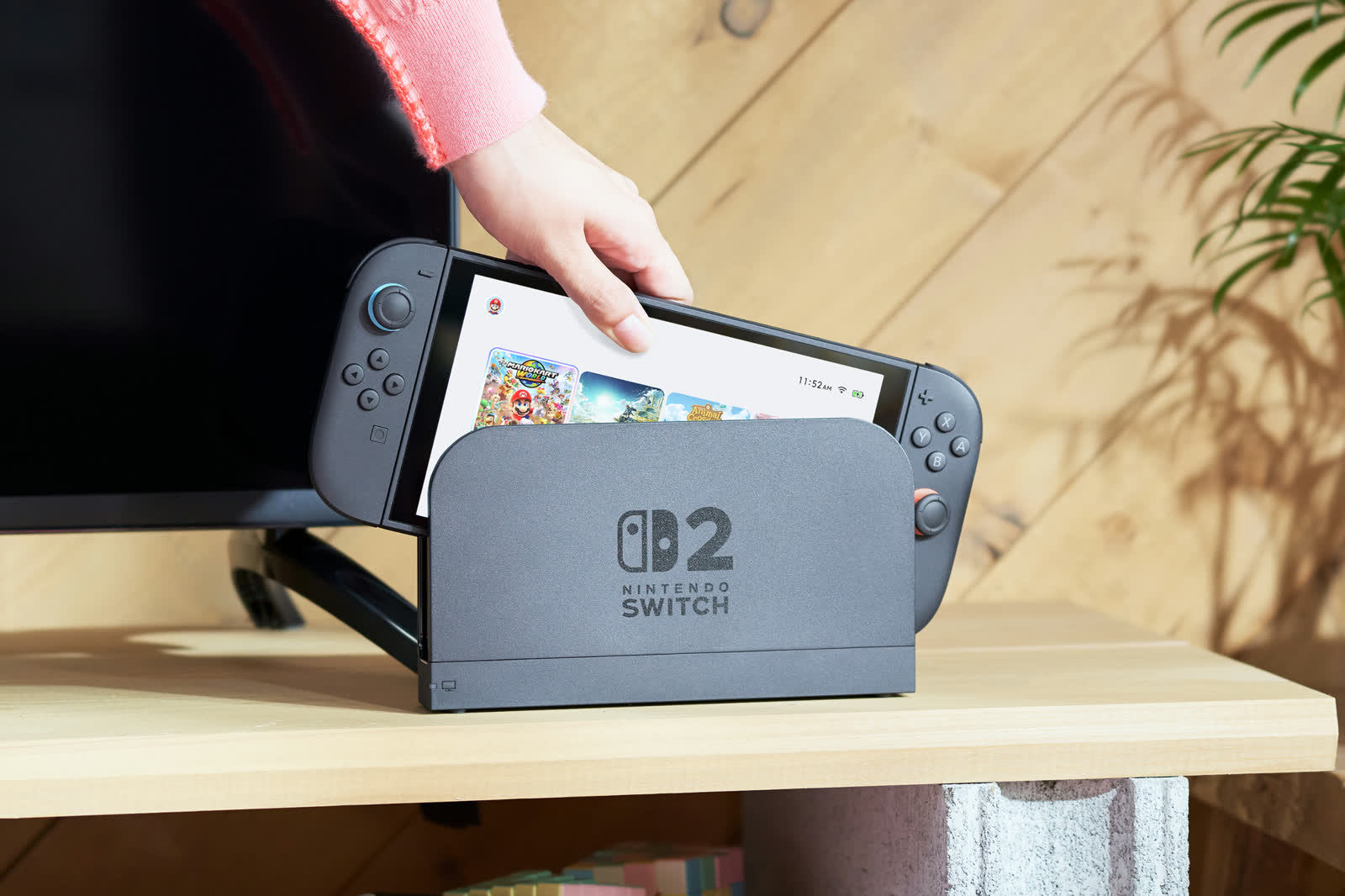 닌텐도 공식 사진 — 책상 위 스탠드에 세워 둔 Nintendo Switch 2와 조이콘 2를 든 손