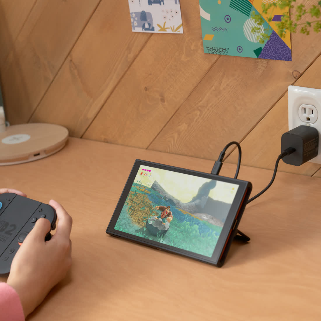 닌텐도 공식 사진 — 책상 위 스탠드에 세워 둔 Nintendo Switch 2와 조이콘 2를 든 손